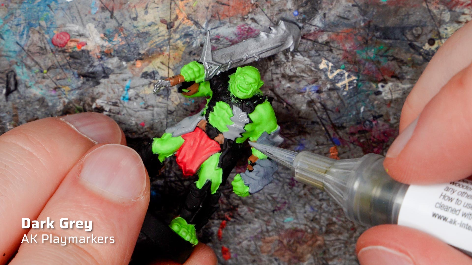 Two hands painting a Heroquest Ork miniature with a dark grey Playmarker from AK