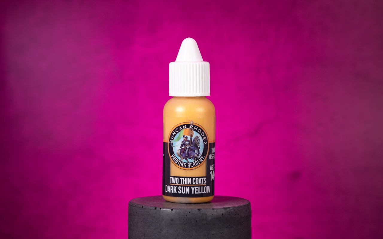 A bottle of Two Thin Coats Dark Sun Yellow on a concrete platform in front of a pink lit background