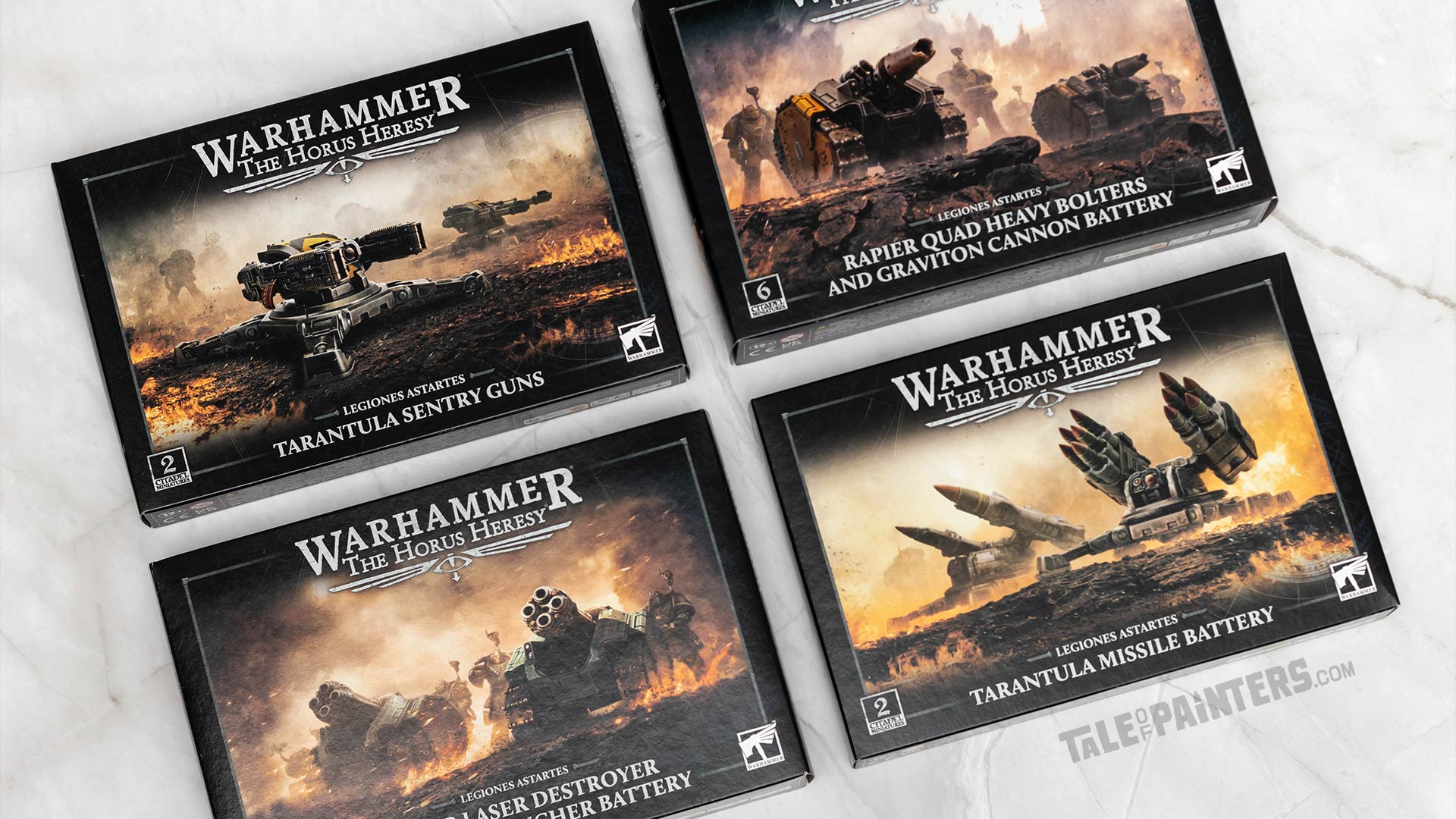 Four Horus Heresy model set boxes arranged on a white marble background, featuring Tarantula Sentry Guns and Missile Battery, and Rapier Quad Heavy Bolter and Graviton Cannon plus Laser Destroyer and Quad Launcher batteries. Photographed for review purposes.