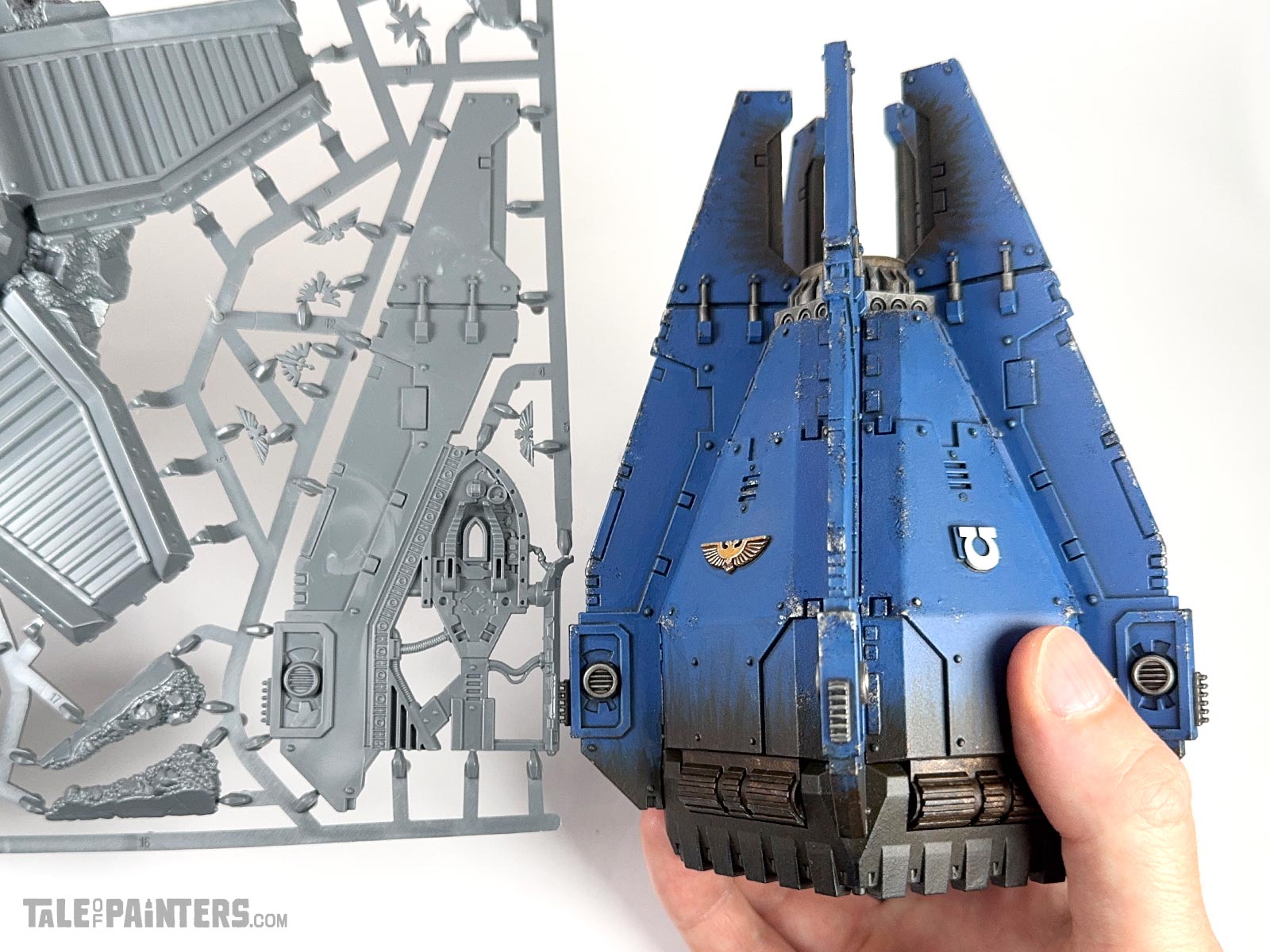 A hand holding an old Space Marines Drop Pod painted blue next to the sprues of the 2025 Drop Pods version