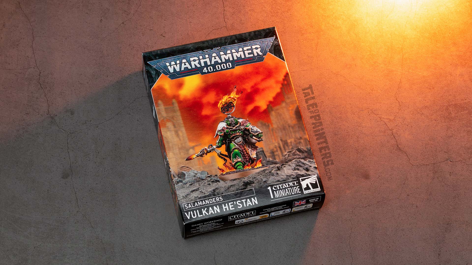 Vulkan He’stan Warhammer 40k model box arranged on a concrete background, lit with orange light, photographed for review purposes