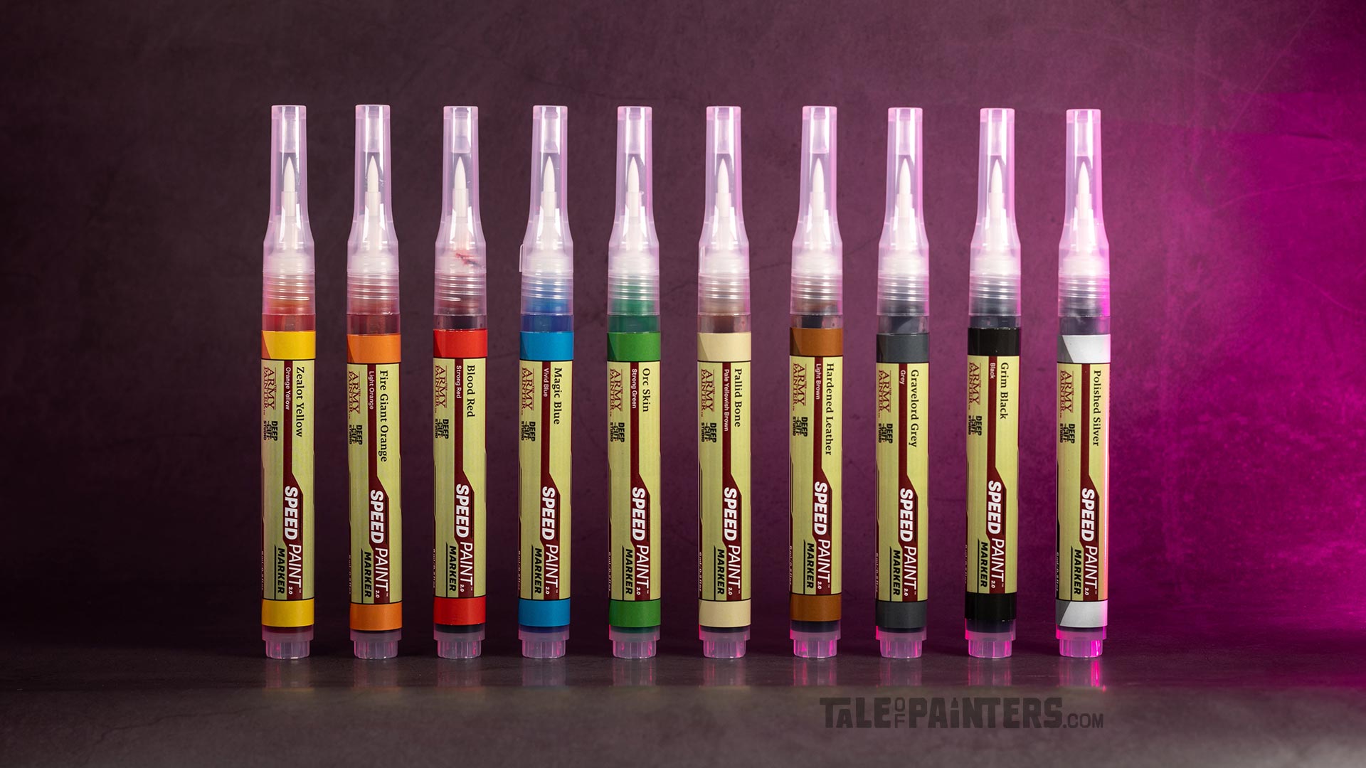 10 Speedpaint markers from The Army Painter, lined up in front of a concrete background lit with pink light, photographed for review purposes