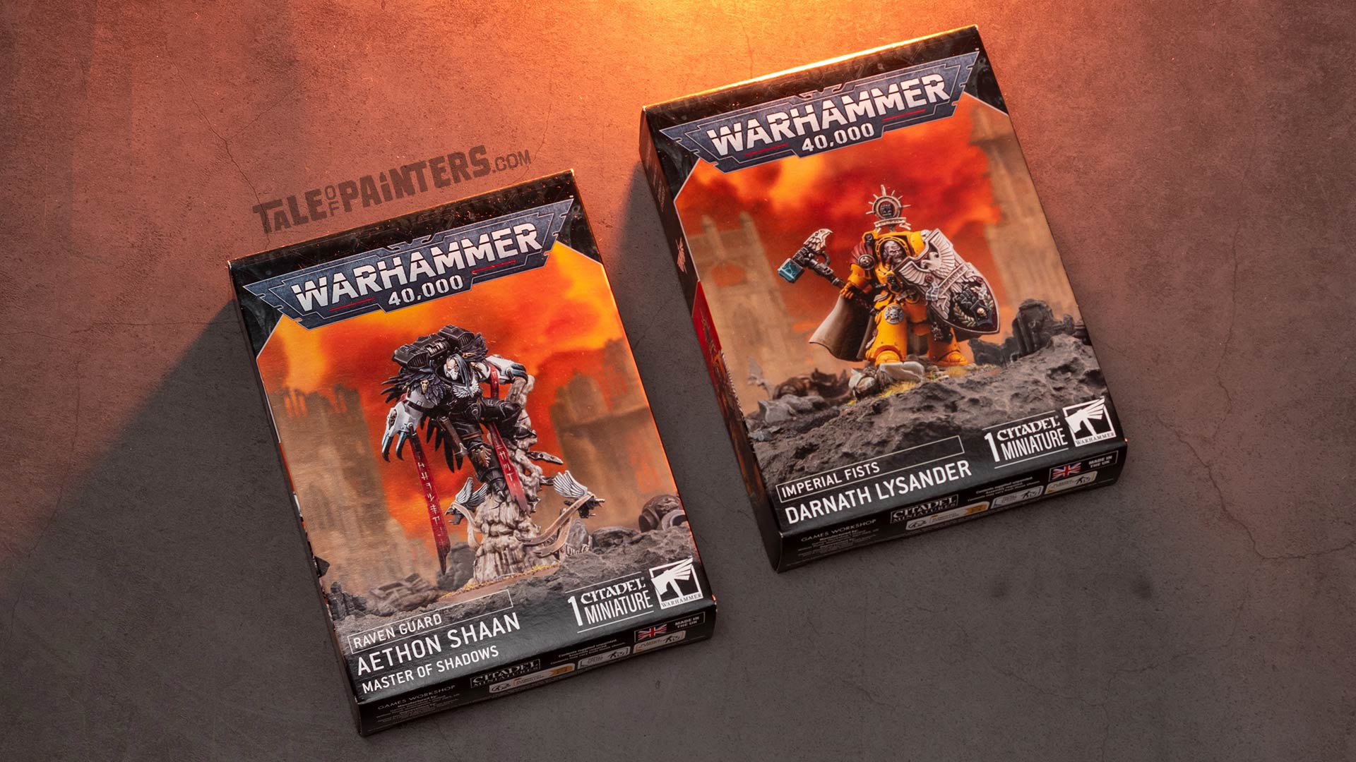 Raven Guard Aethon Shaan and Imperial Fists Darnath Lysander model kit boxes arranged on a concrete background, lit with orange light, photographed for review purposes