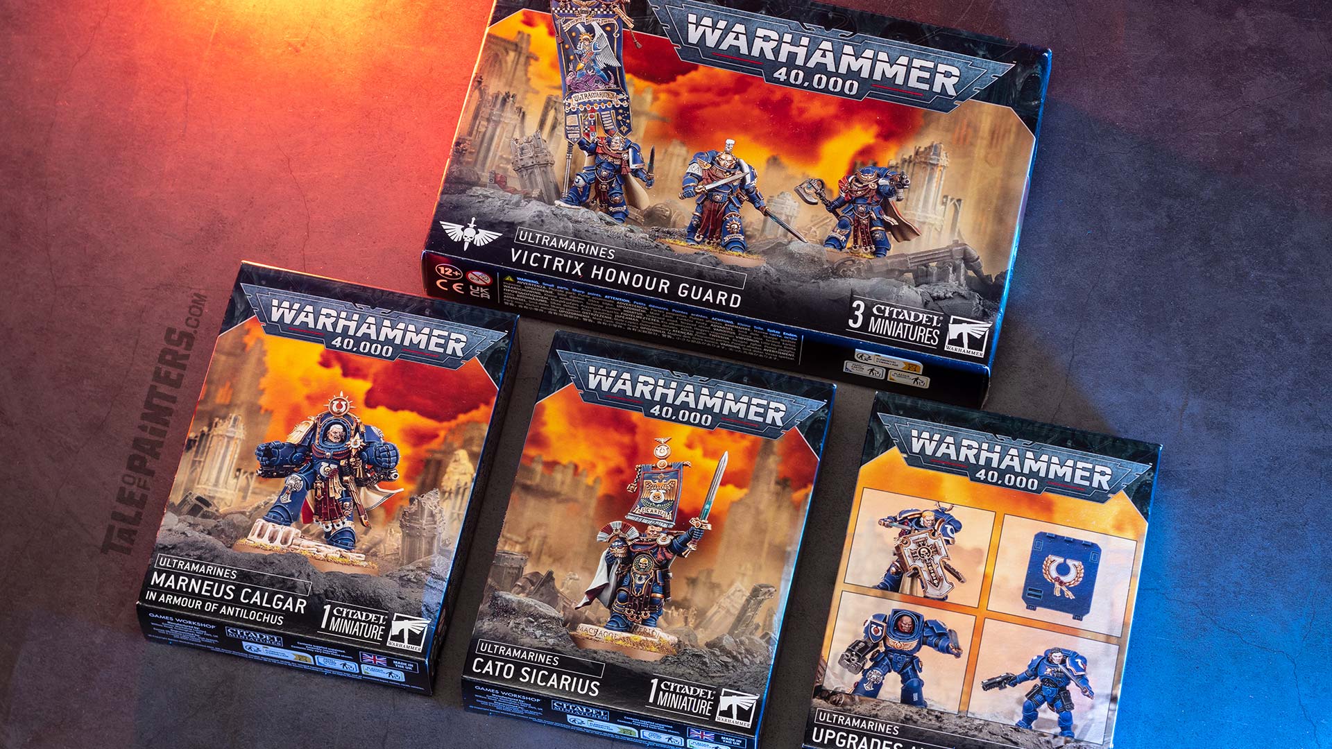 Ultramarines Victrix Guard, Marneus Calgar in Armour of Antilochus, Cato Sicarius, and Ultramarines Upgrades and Transfers boxes on a concrete background, lit with orange and blue light