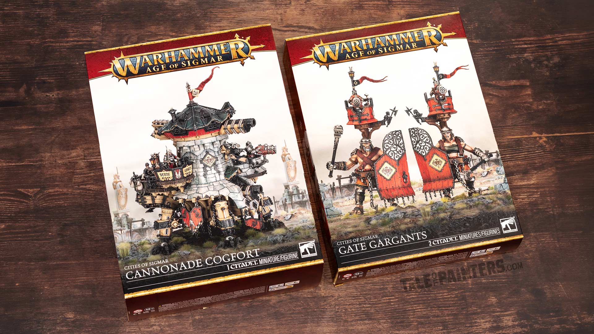 Cities of Sigmar Cannonade Cogfort and Gate Gargants model kit boxes for the Warhammer Age of Sigmar game, arranged on a wooden background