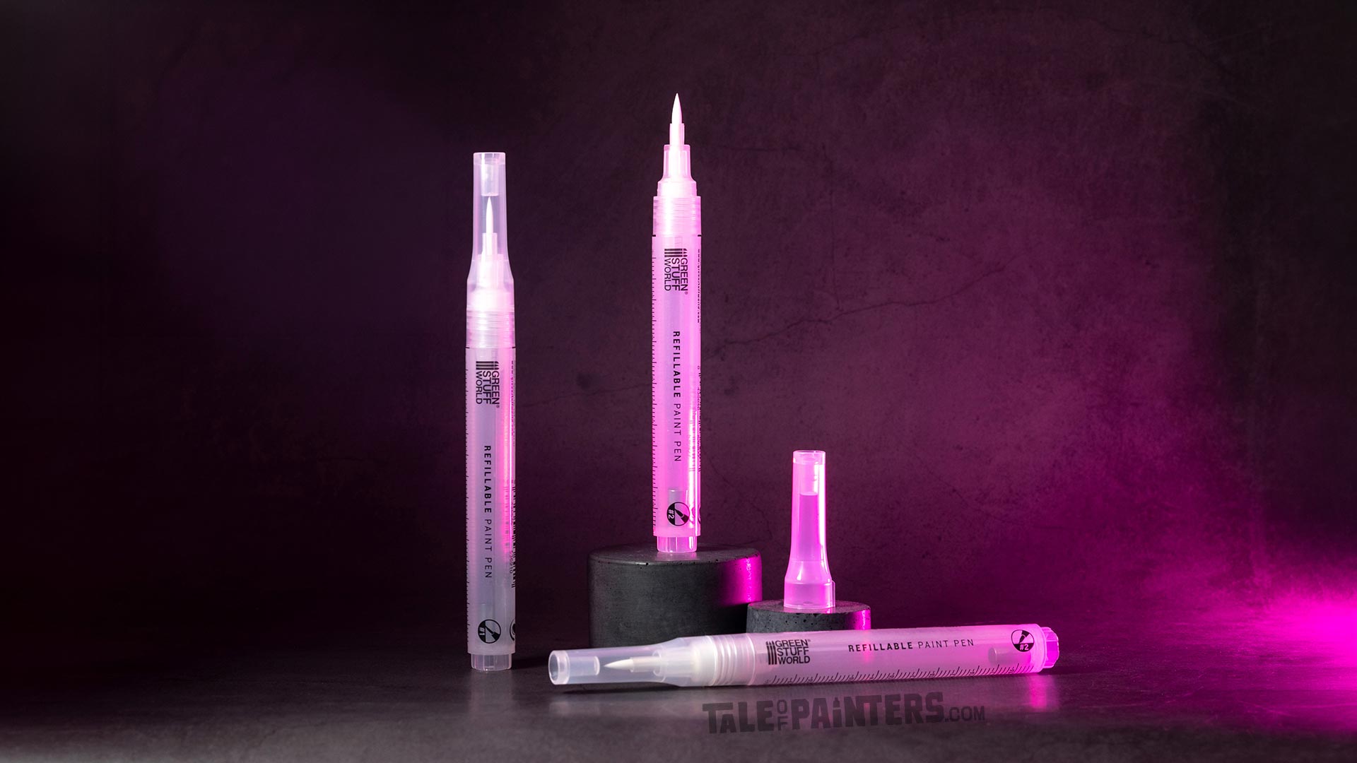An arrangement of three empty refillable paint markers from Green Stuff World, lit with dramatic pink light, on a dark concrete background