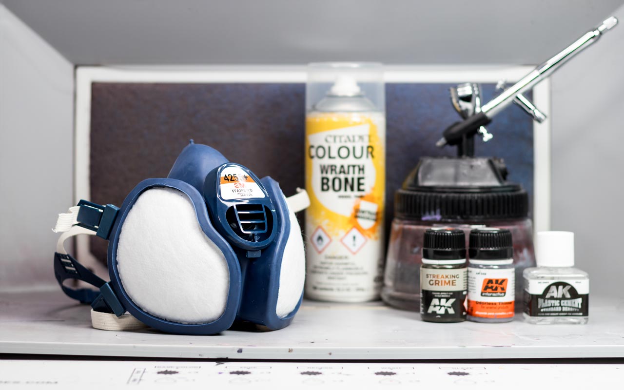 A 3M respirator mask next to a Warhammer Colour Wraithbone spray can, airbrush, and AK Streaking Grime and thinner