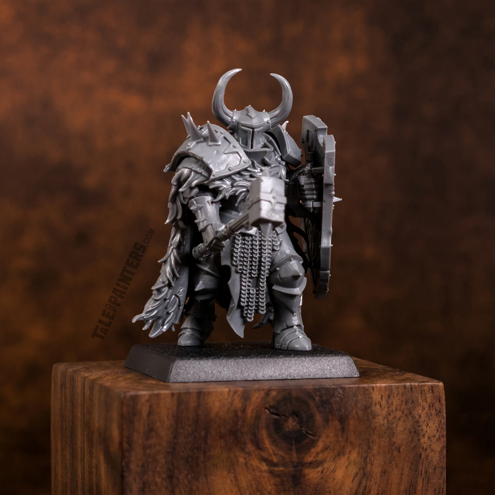 An assembled Old World Chaos Warrior model from 2026 with hammer and shield, on a dark wooden plinth, dark brown background